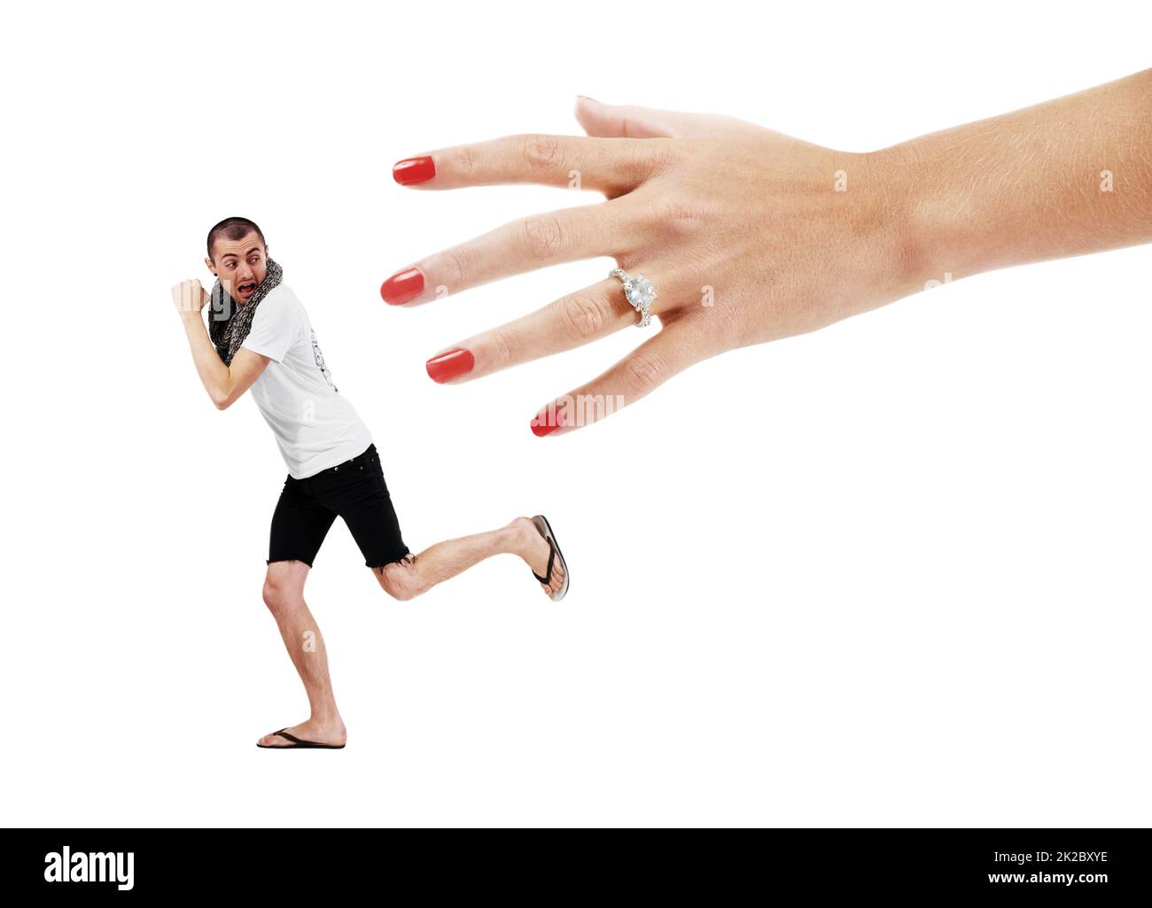 Angst vor Engagement. Ein junger Mann, der versucht, einer riesigen Hand mit einem Ehering zu entfliehen. Stockfoto