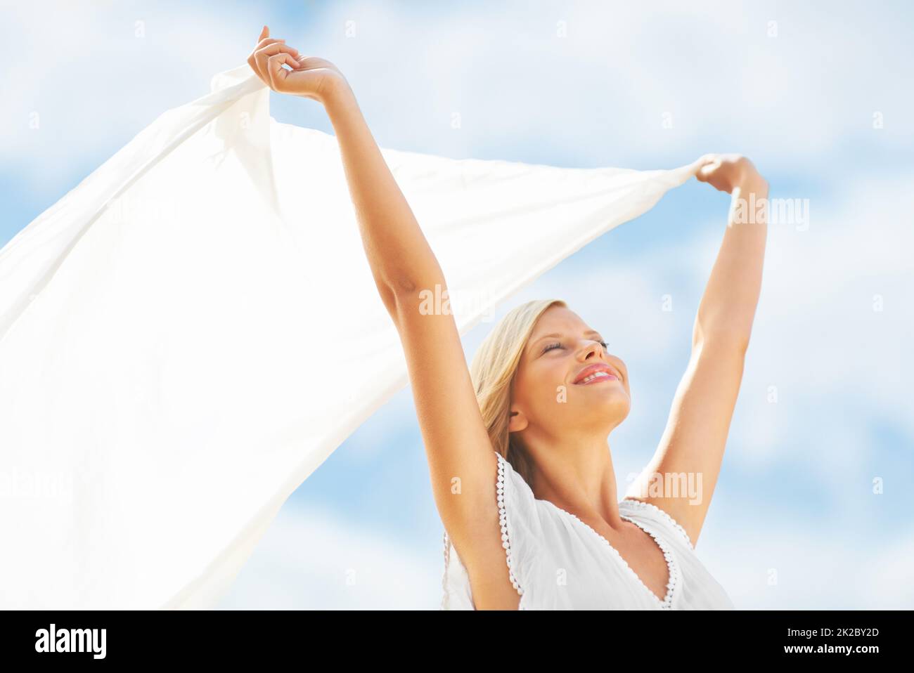 Sich mit vitaler Energie lebendig fühlen. Eine schöne junge Frau, die einen Schal in der Brise hält. Stockfoto