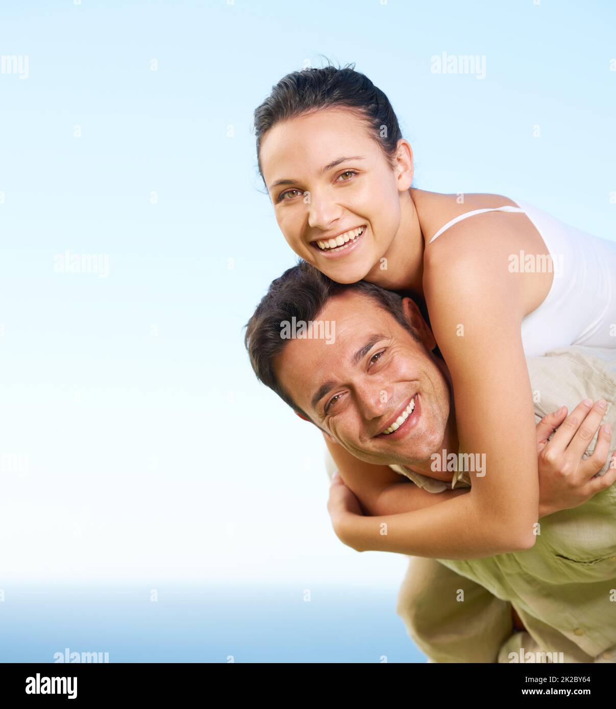 Wir haben ihren Urlaub genossen. Ein junger Mann, der seiner Freundin einen Huckepack mit dem Ozean im Hintergrund gibt. Stockfoto