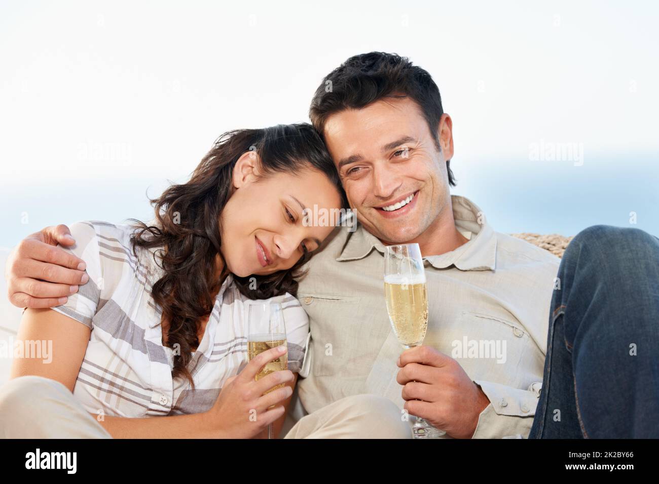 Wir feiern ihre Liebe. Ein süßes Paar, das Champagner mit dem Meer im Hintergrund trinkt. Stockfoto