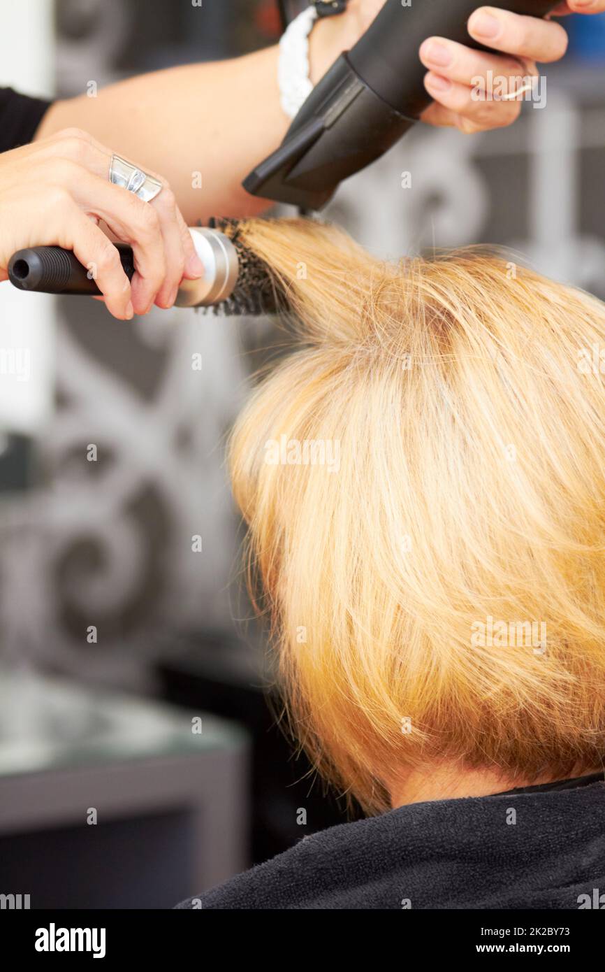 Perfektionieren jeder Haarsträhne. Eine blonde Frau, die ihre Haare beim Friseur getrocknet bekommt. Stockfoto