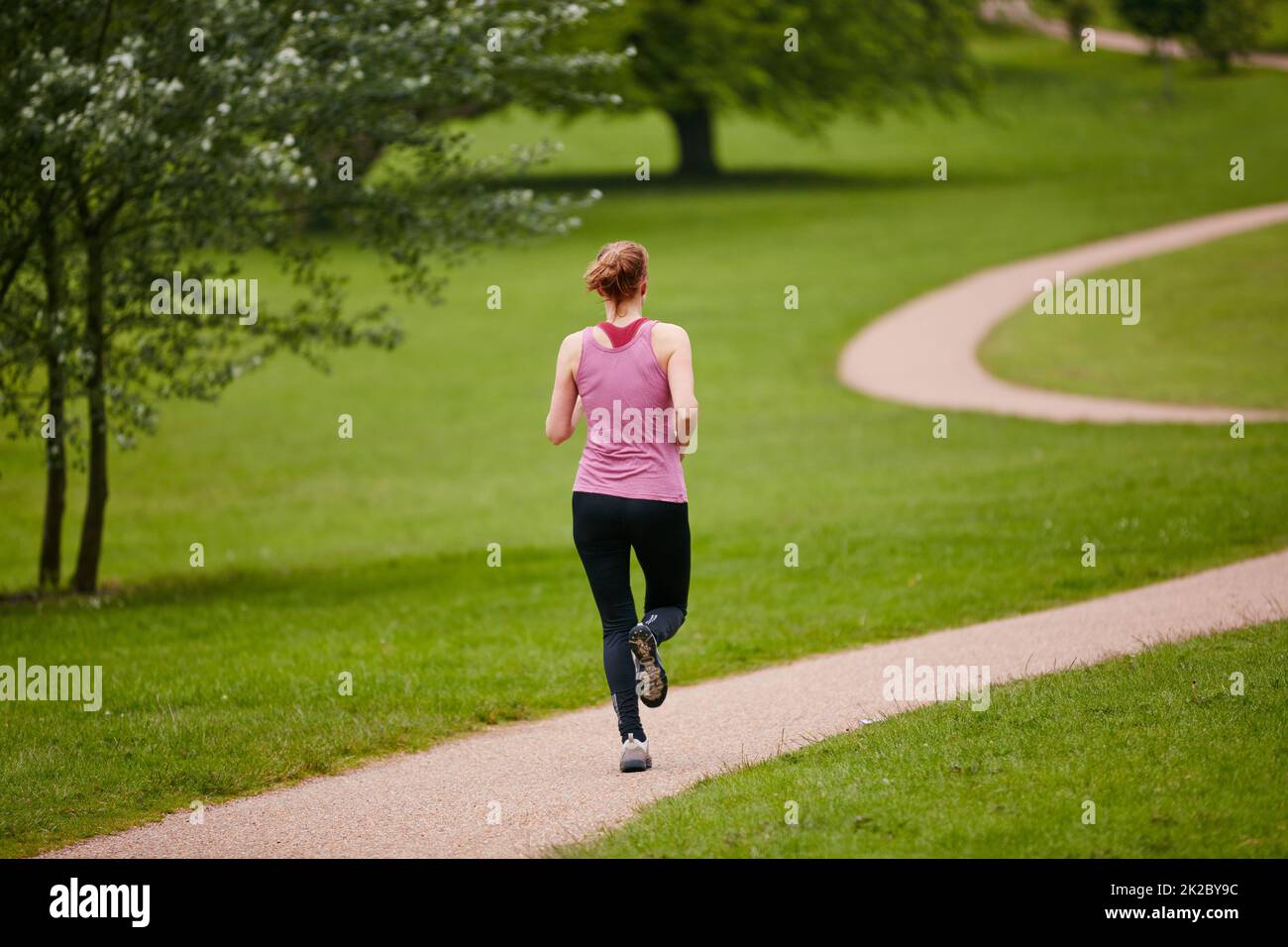 Nur sie und der Weg. Rückansicht einer Frau, die in einem Park entlang eines Fußwegs joggt. Stockfoto