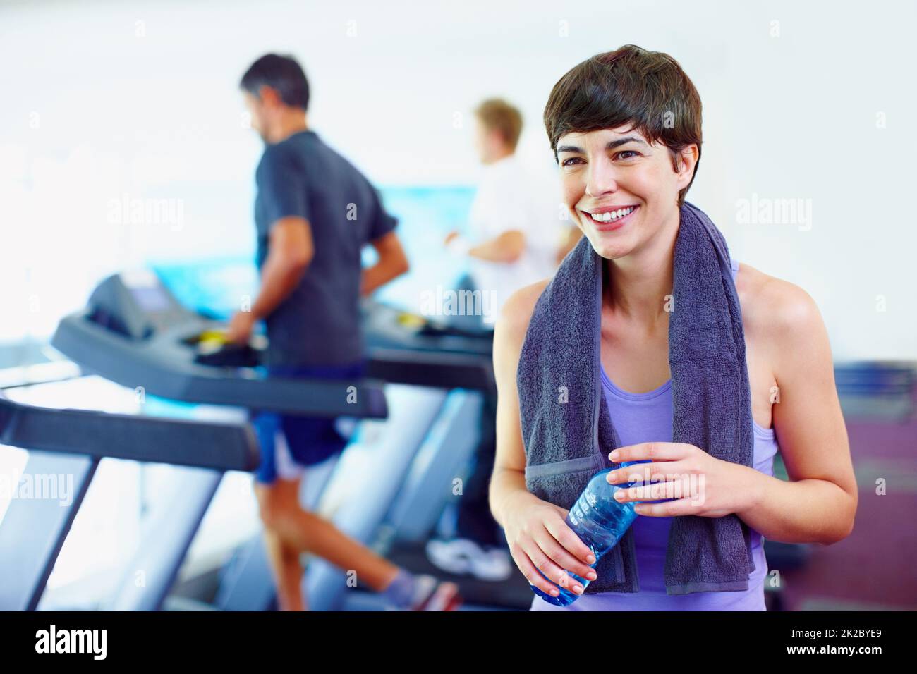 Frau mit einer Flasche Wasser. Lächelnde Frau mit einer Flasche Wasser und Blick weg mit Menschen arbeiten im Hintergrund. Stockfoto