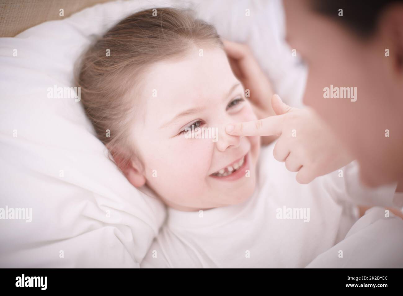 Schlafenszeit-Affektionen. Nahaufnahme einer Mutter, die ihre lächelnde junge Tochter ins Bett legt. Stockfoto