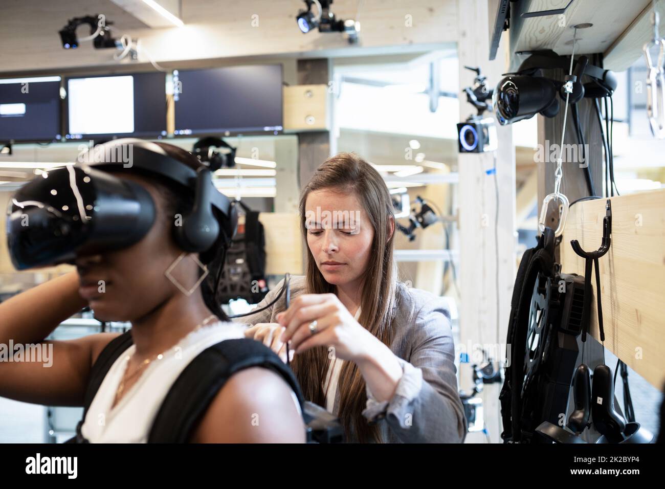 Frau, die Kollegen mit Kopfbedeckungen für virtuelle Realität unterstützt Stockfoto