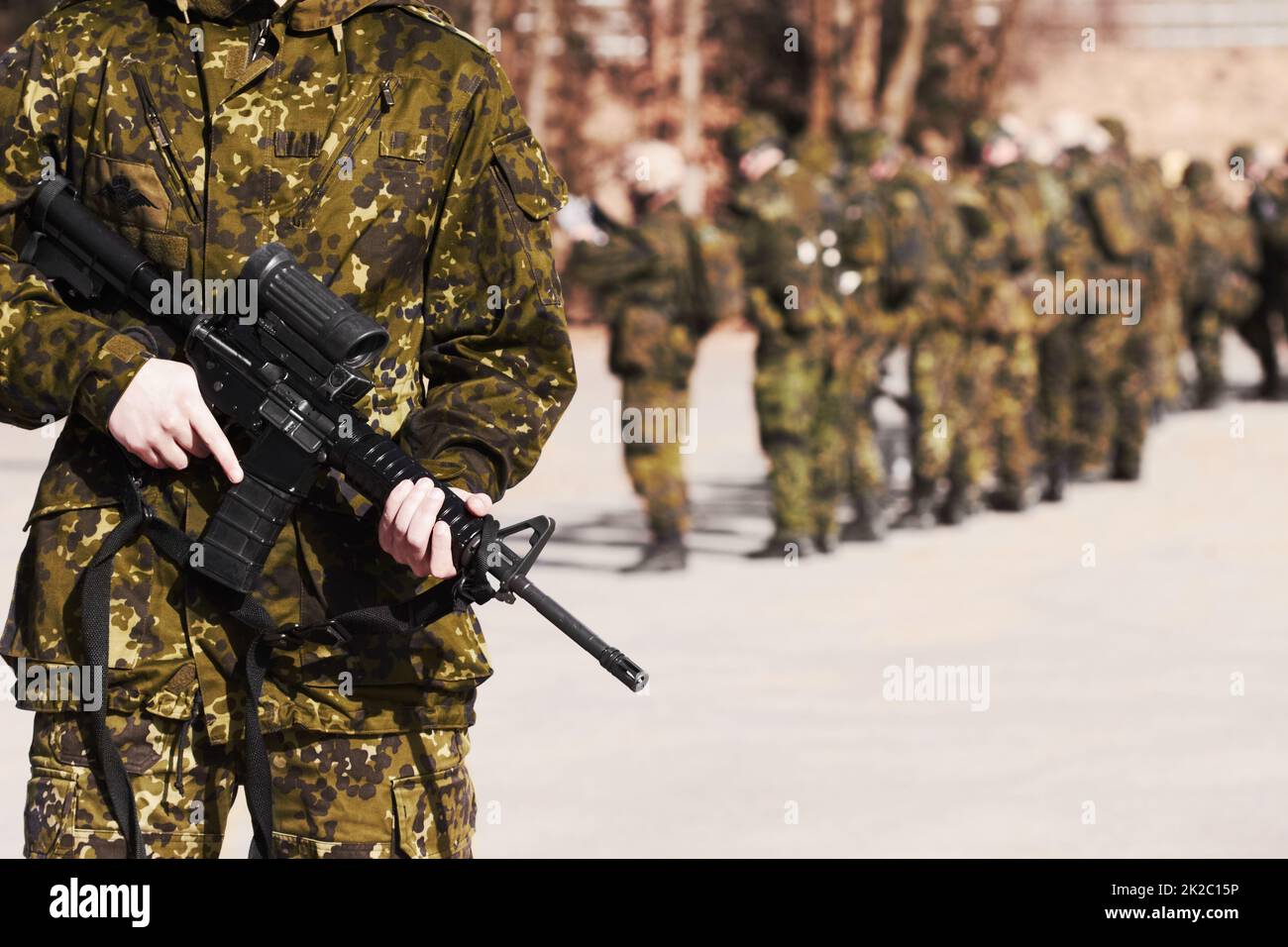 Bereit für alles. Ein Soldat, der mit einem Gewehr steht, und seine Mitsoldaten im Hintergrund. Stockfoto