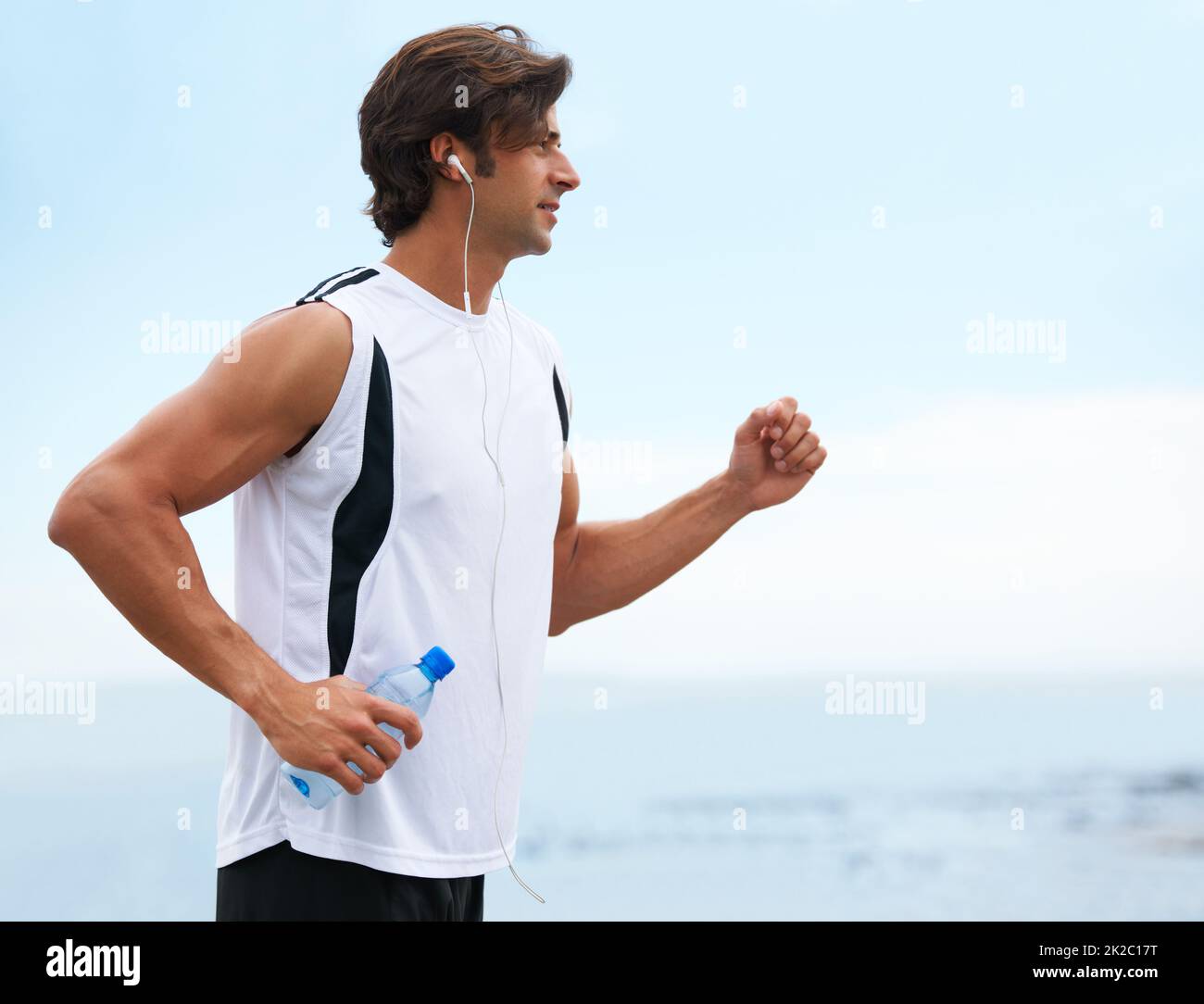 Nichts kann ihn zurückhalten. Profilansicht eines gutaussehenden Mannes, der eine Wasserflasche hält, laufen geht und Musik hört - Copyspace. Stockfoto