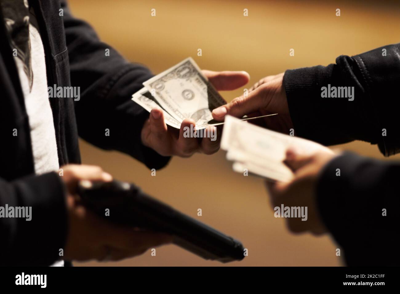 Abschluss des Geschäfts. Hände, die Bargeld halten, und eine Waffe, die Geld zwischen ihnen weitergibt. Stockfoto