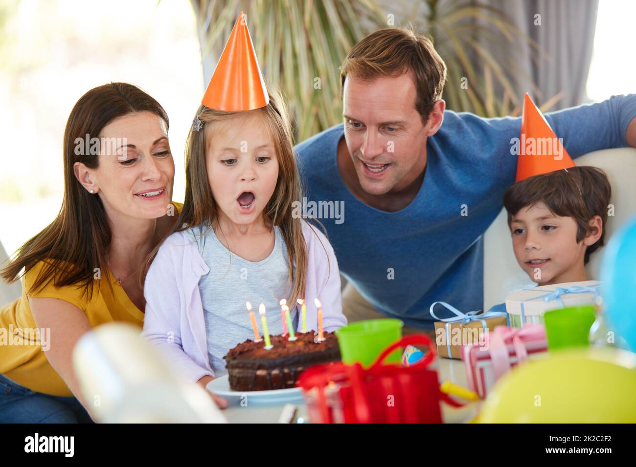 Der Moment, auf den sie alle gewartet haben. Aufnahme eines kleinen Mädchens, das die Kerzen ihres Geburtstagstortes umringt von ihrer Familie ausbläst. Stockfoto