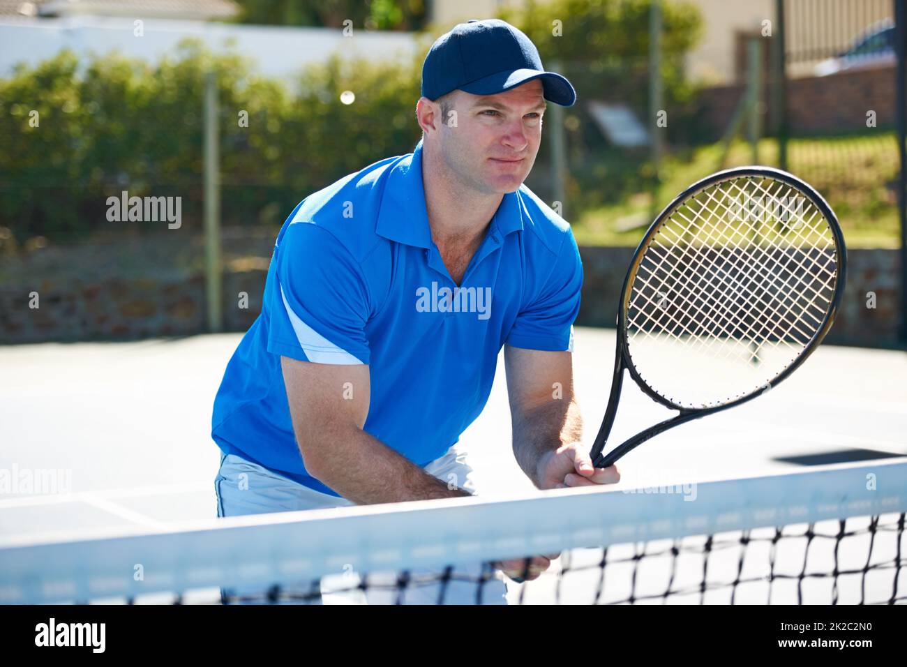 Das Netz schützen. Ein männlicher Tennisspieler, der am Netz steht und auf den Gegenschuss wartet. Stockfoto