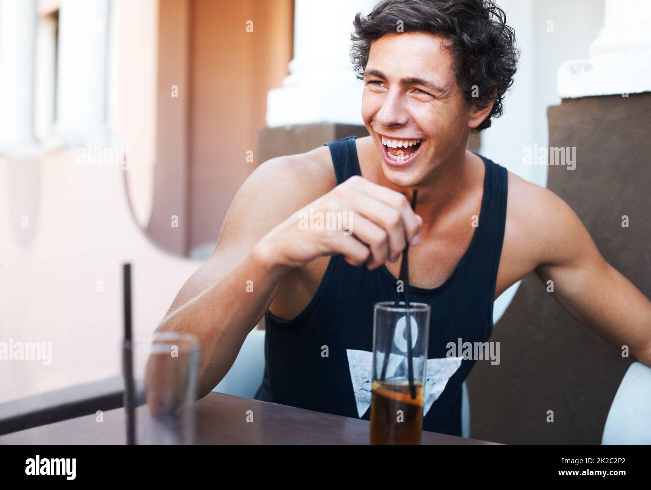 Dieser Witz war urkomisch. Hübscher junger Mann, der lachend sein kaltes Getränk genießt. Stockfoto