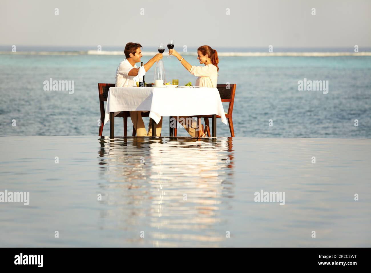 Alles Gute zum Jahrestag. Ein glückliches Paar, das ihre Weingläser anklimmelte, während es draußen, umgeben von Wasser, saß. Stockfoto