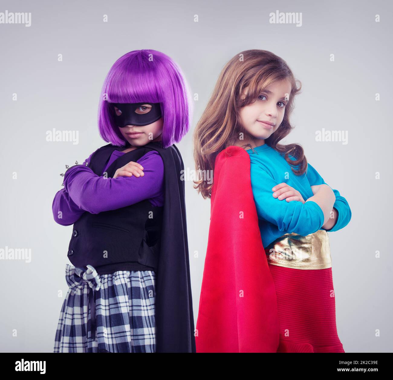 Nicht jedes Mädchen will eine kleine Prinzessin sein. Eine Studioaufnahme von zwei kleinen Mädchen, die als Superhelden und Bösewicht verkleidet sind. Stockfoto
