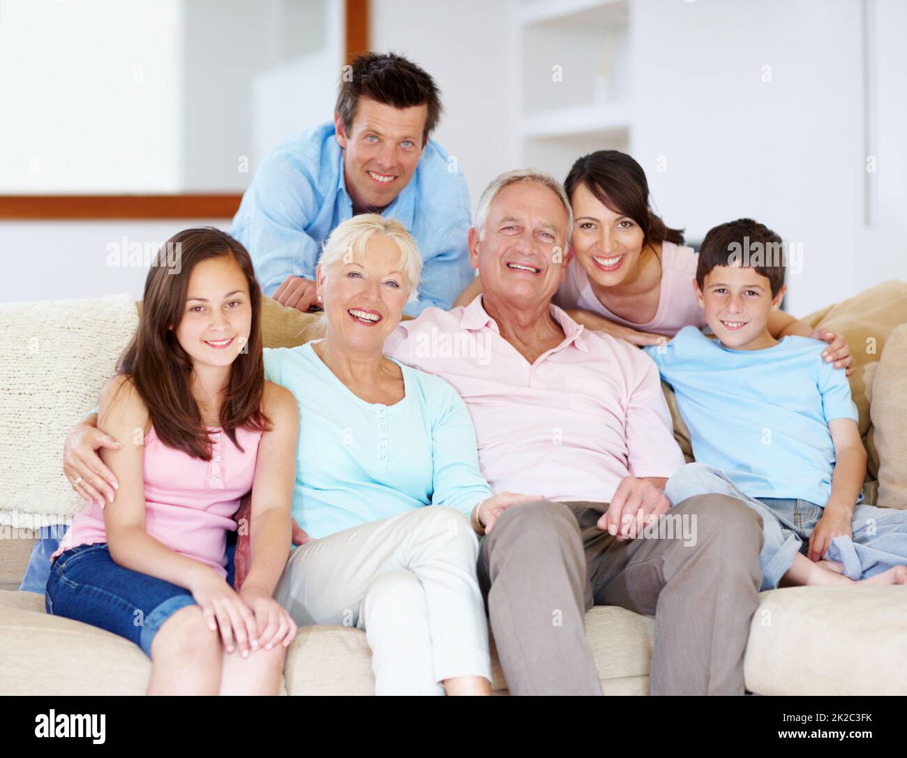 Gemeinsam durch das Leben gehen - Familienunterstützung. Drei Generationen Familie sitzen liebevoll auf der Loungecouch zusammen. Stockfoto