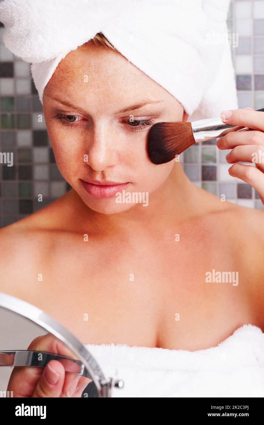 Nette Frau, die sich selbst an der Hand Spiegel und Anwendung Make-up. Schöne junge weibliche Blick auf sich selbst an der Hand Spiegel und Anwendung Make-up. Stockfoto