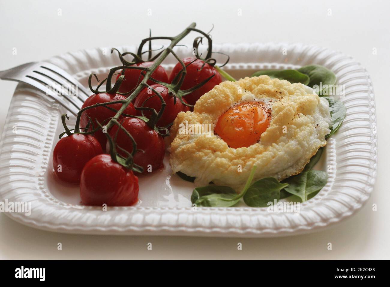 Gesundes Frühstück mit Cloud Ei, spinash und Cherry Tomaten. Wolken ist eine Ofenform, wenn das Eiweiß und Eigelb getrennt kochen Stockfoto