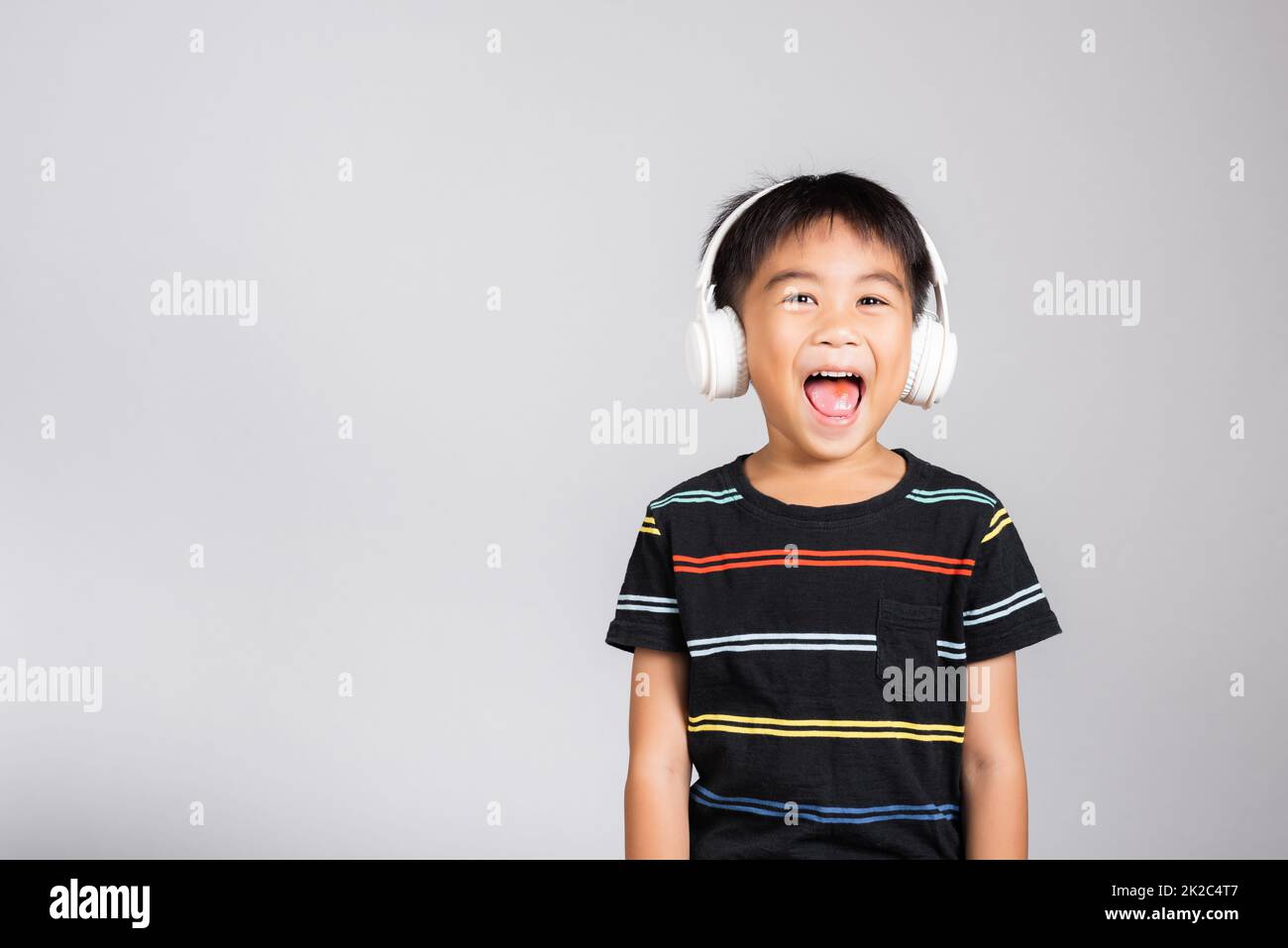 Kleiner, süßer Junge, 5-6 Jahre alt, hört Musik und trägt kabellose Kopfhörer im Studio isoliert Stockfoto