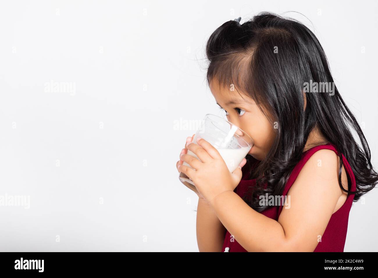 Ein süßes Mädchen, 3-4 Jahre alt, lächelt mit Milchglas, trinkt weiße Milch Stockfoto