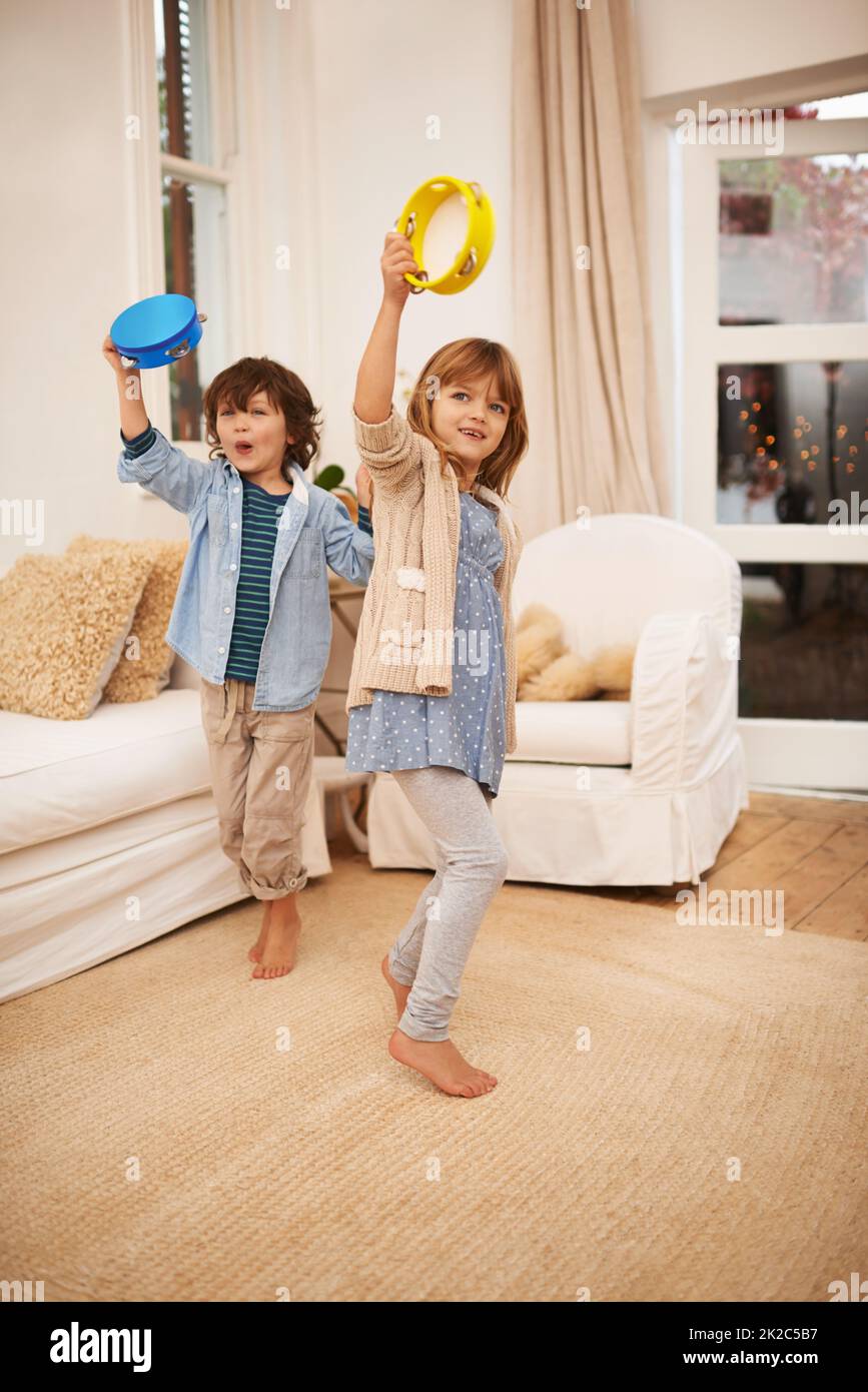 Spaß mit Musik machen. Aufnahme von zwei kleinen Kindern, die im Wohnzimmer zu Hause mit Tamburinen spielen. Stockfoto