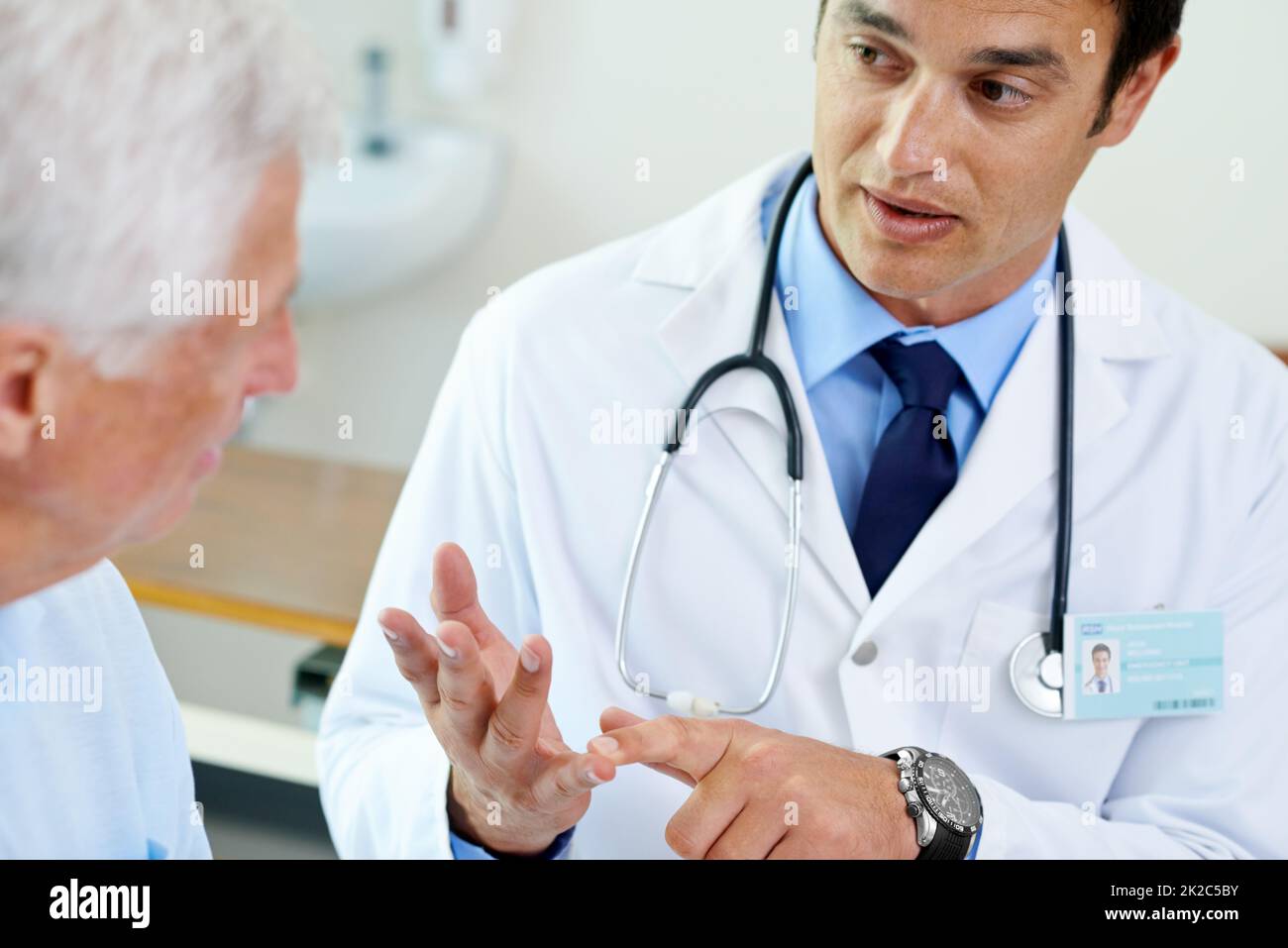 Sicherstellen, dass sein Patient versteht Aufnahme eines hübschen jungen Arztes, der einem älteren Patienten die Situation erklärt. Stockfoto