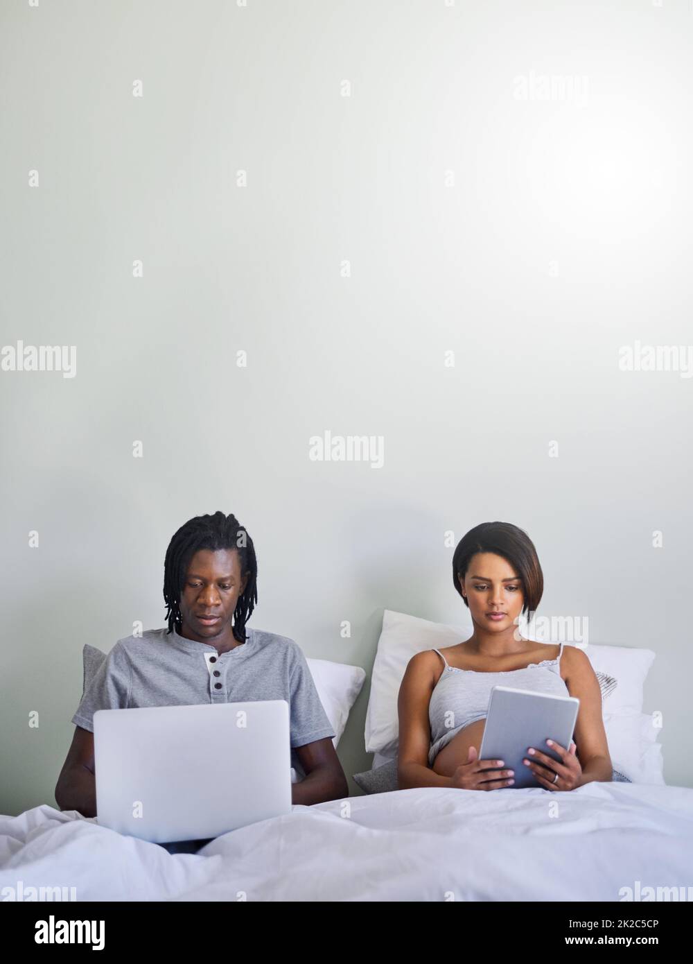 Glauben Sie nicht alles, was Sie online lesen. Aufnahme eines Paares, das im Bett sitzt, während es drahtlose Geräte verwendet. Stockfoto