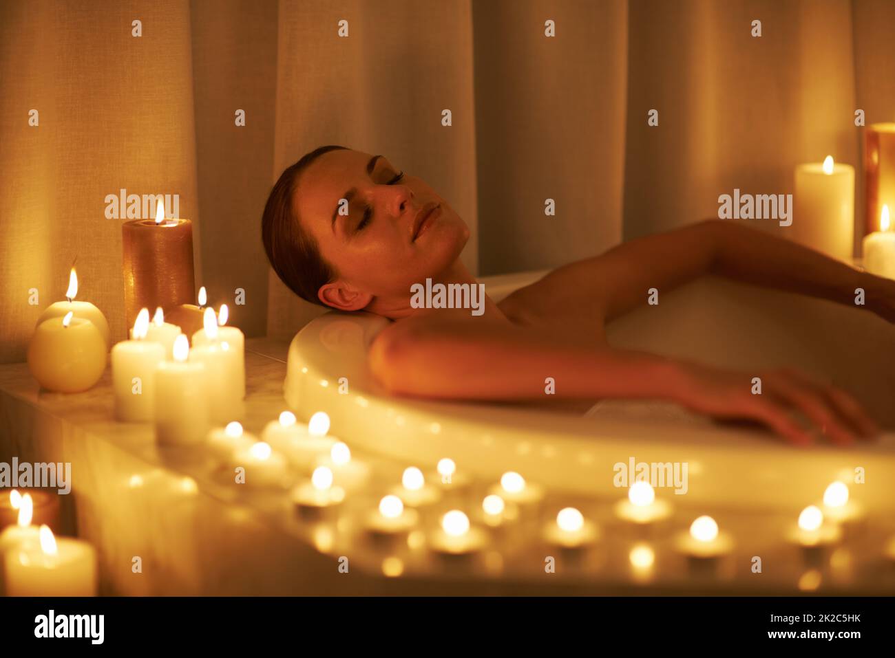 Die Sorgen der Wochen wuschen weg. Eine kurze Aufnahme einer wunderschönen Frau, die sich in einem bei Kerzenschein beleuchteten Bad entspannt. Stockfoto