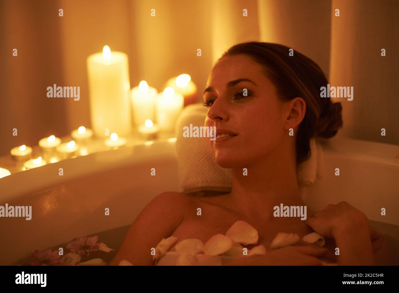 Beruhigt durch das Ambiente und ein heißes Bad. Eine kurze Aufnahme einer wunderschönen Frau, die sich in einem bei Kerzenschein beleuchteten Bad entspannt. Stockfoto