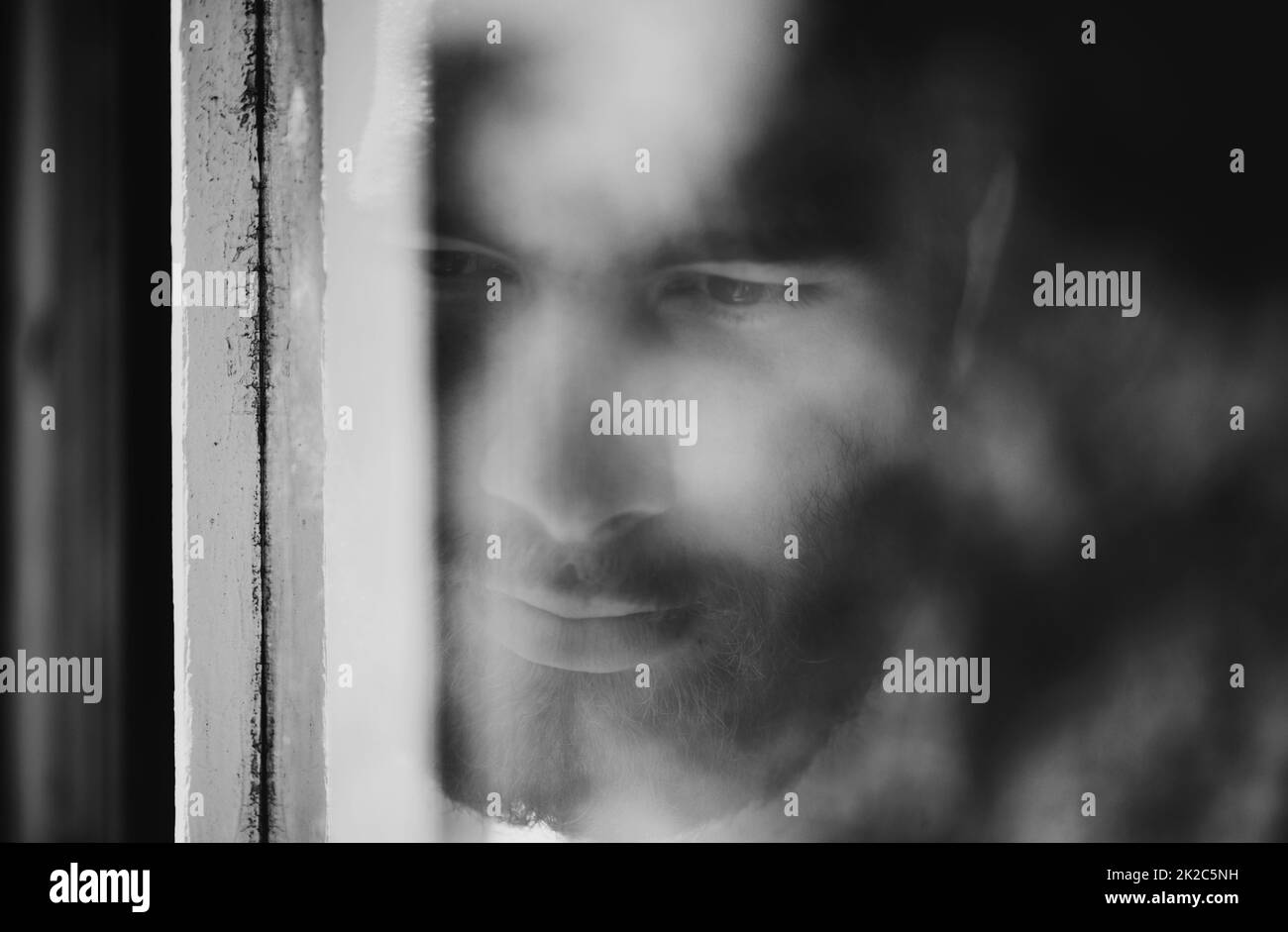 Verschwommener Blickpunkt. Nahaufnahme eines nachdenklichen jungen Mannes, der durch ein Fenster gesehen wird. Stockfoto