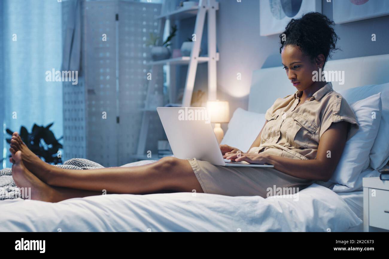 Zeit für ein paar nächtliche Bloggen. Aufnahme einer attraktiven jungen Frau, die ihren Laptop benutzt, während sie nach einem langen Arbeitstag auf ihrem Bett lag. Stockfoto
