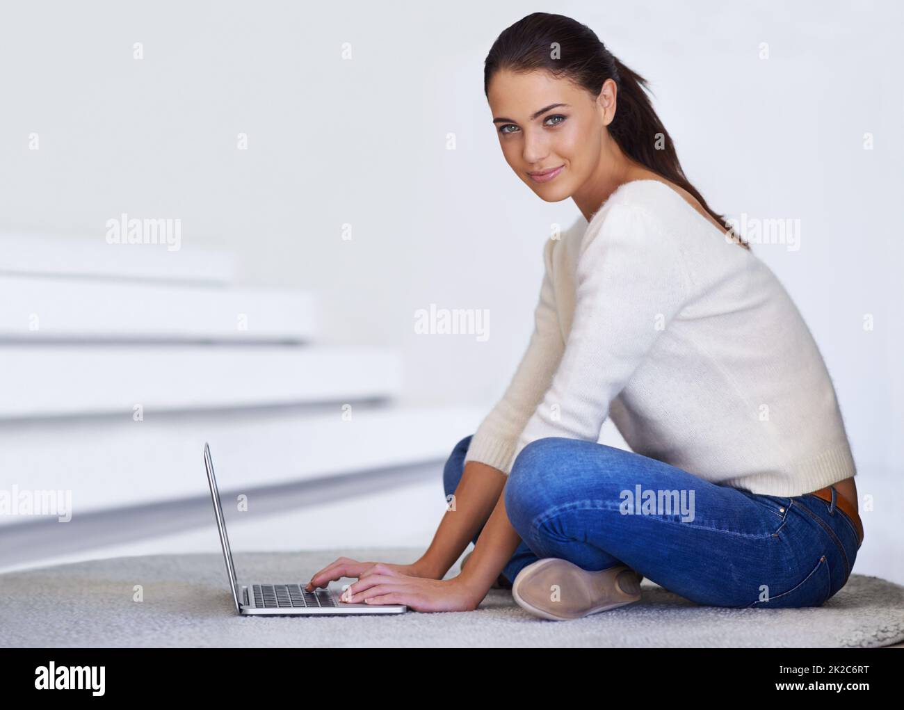 Komfortable Konnektivität. Eine schöne junge Frau, die auf ihrem Boden sitzt und einen Laptop benutzt. Stockfoto