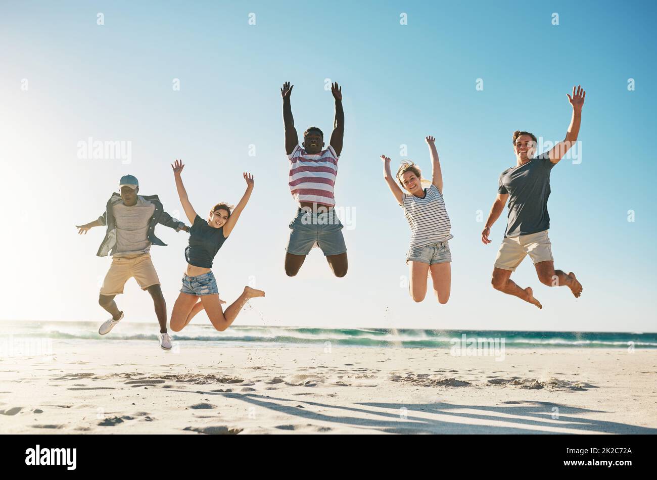 Lösen Sie sich mit Ihren besten Freunden. Aufnahme einer Gruppe junger Freunde, die am Strand begeistert in die Luft springen. Stockfoto