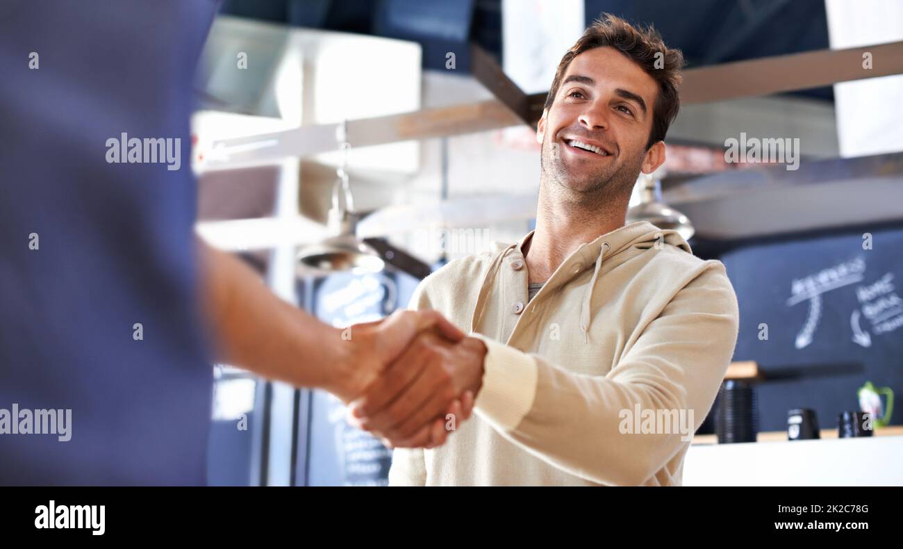 Zu einem alten Freund rennt. Ein junger Mann schüttelt sich bei einem Coffeeshop mit einem Freund die Hände. Stockfoto