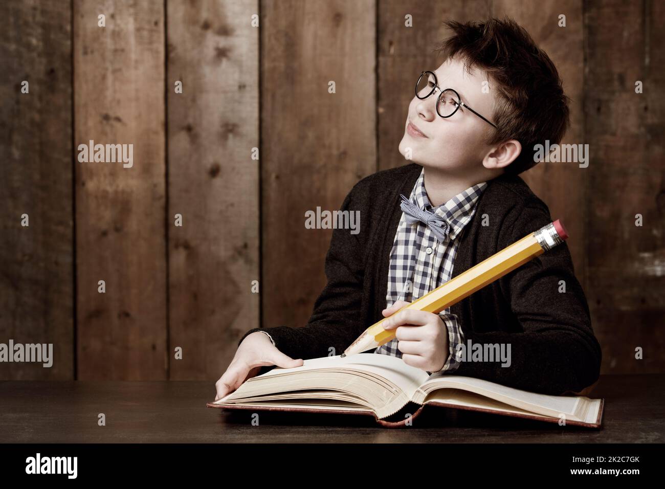 Schreiben Sie einige große Ideen auf. Kleiner Junge mit Brille und Hausaufgaben mit einem riesigen Bleistift. Stockfoto