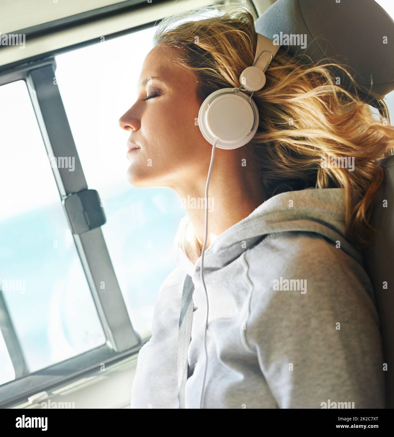 Lassen Sie ihre Sorgen wegtreiben Aufnahme einer Frau in einem Auto, die ihre Augen stillt, während der Wind durch ihre Haare weht und sie Musik hört. Stockfoto