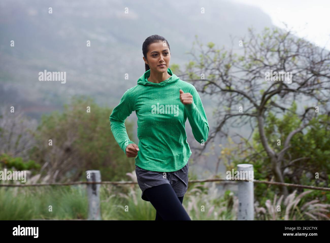 Sie schreitet jeden Tag in ihrer Fitness voran. Eine junge Frau sprintet an einem frischen Morgen entlang einer Bergstraße. Stockfoto