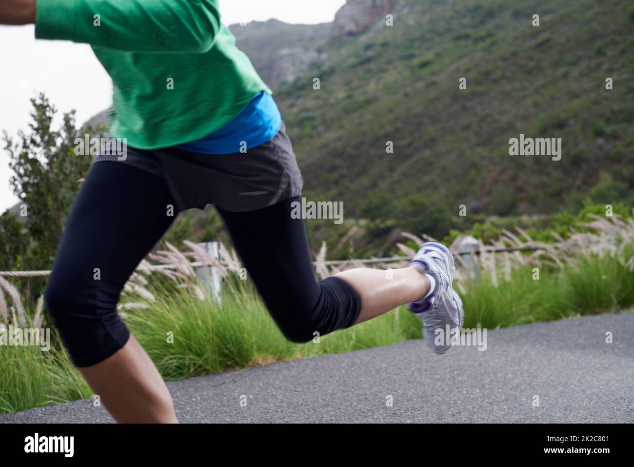Auf die Steigung. Ein kurzer Schuss einer Frau, die an einem knackigen Morgen entlang einer Bergstraße sprintet. Stockfoto
