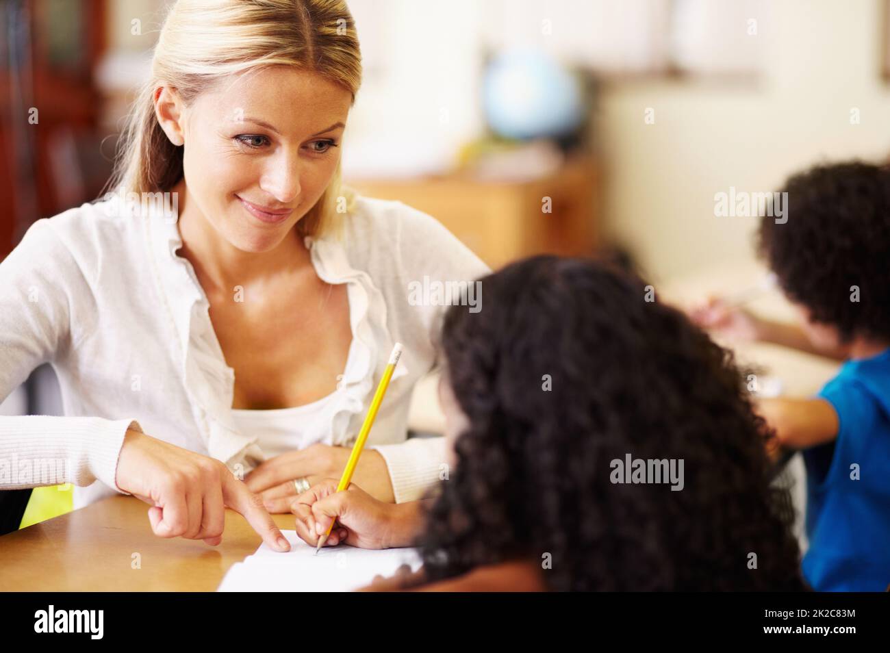 Ihre kleinen Freunde helfen. Eine junge Lehrerin, die Kindern bei ihrer Arbeit hilft. Stockfoto