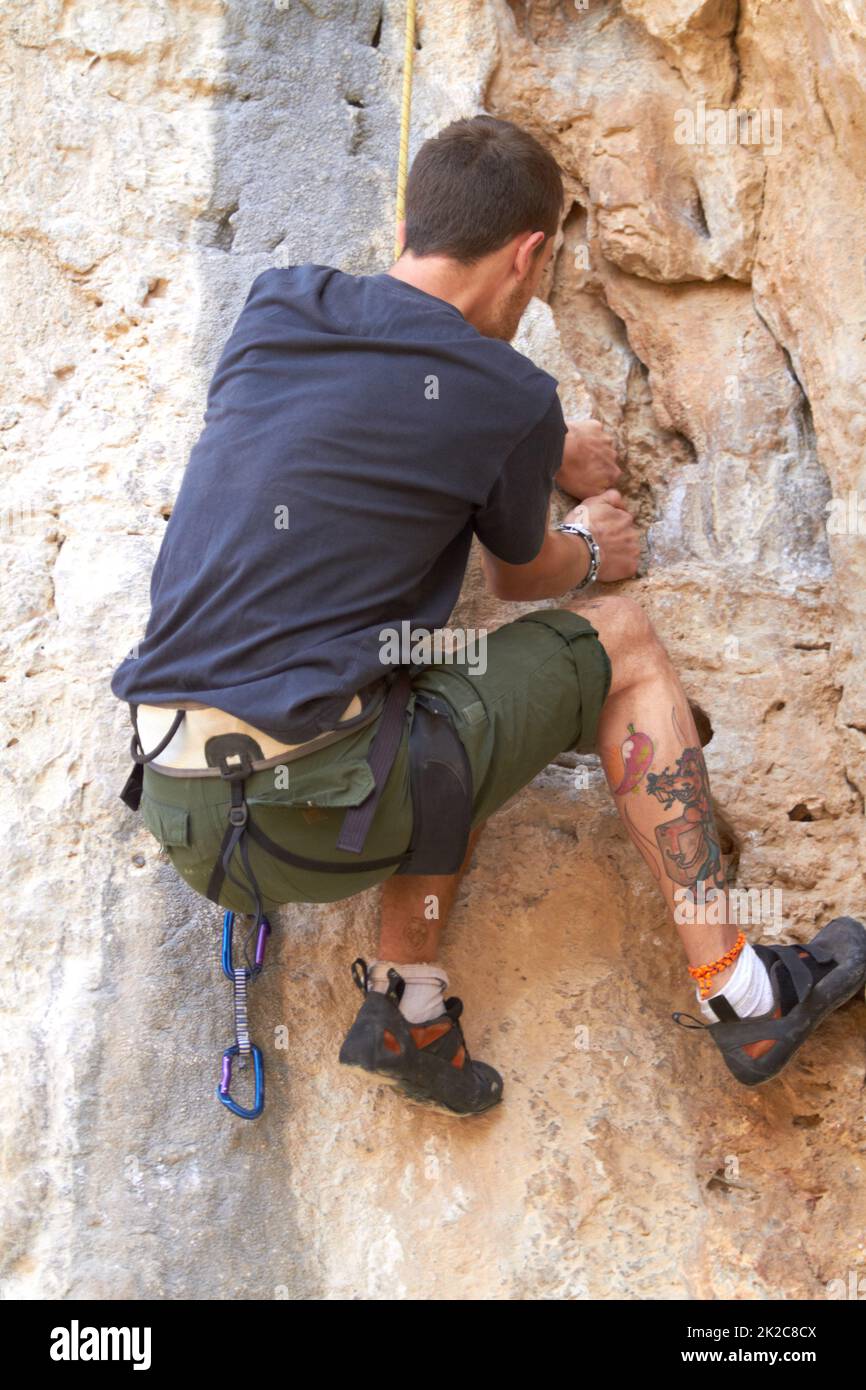 Rockstar des Felskletterns. Rückansicht eines tätowierten Felskletterners, der sich an einem Riss in der Felswand festklammert. Stockfoto