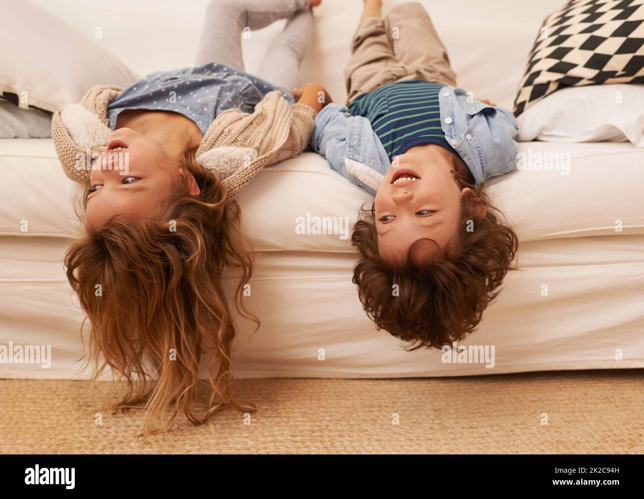 Herumhängen, ohne etwas zu tun. Aufnahme von zwei kleinen Kindern, die auf einem Sofa liegen und ihre Köpfe über dem Rand hängen. Stockfoto