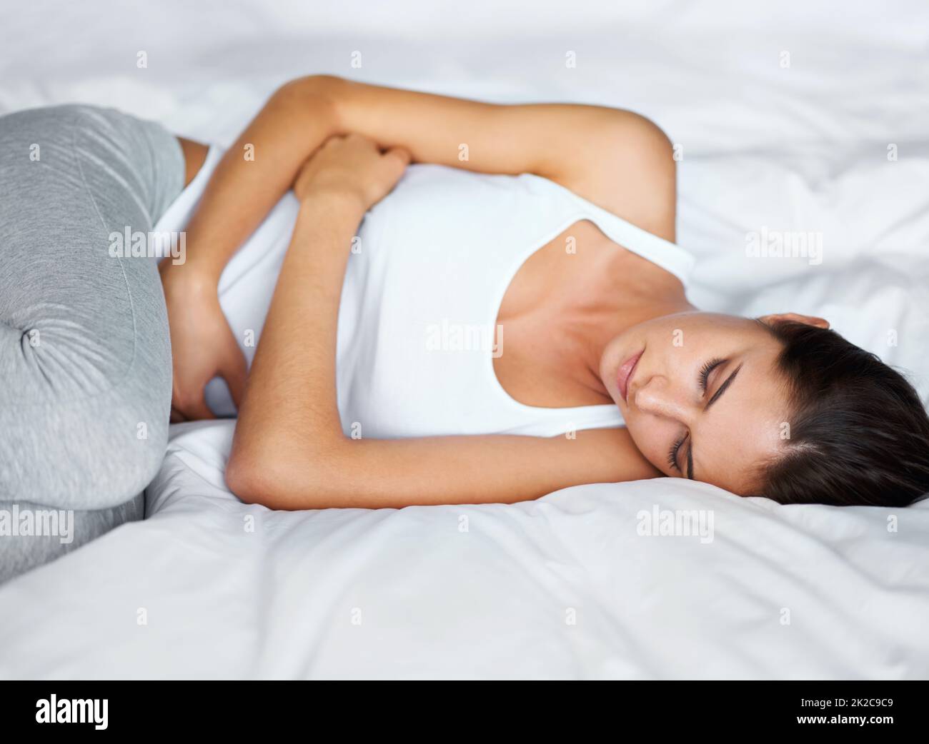 Fühlt sich nicht so toll an. Eine junge Frau, die mit Krämpfen im Bett liegt. Stockfoto