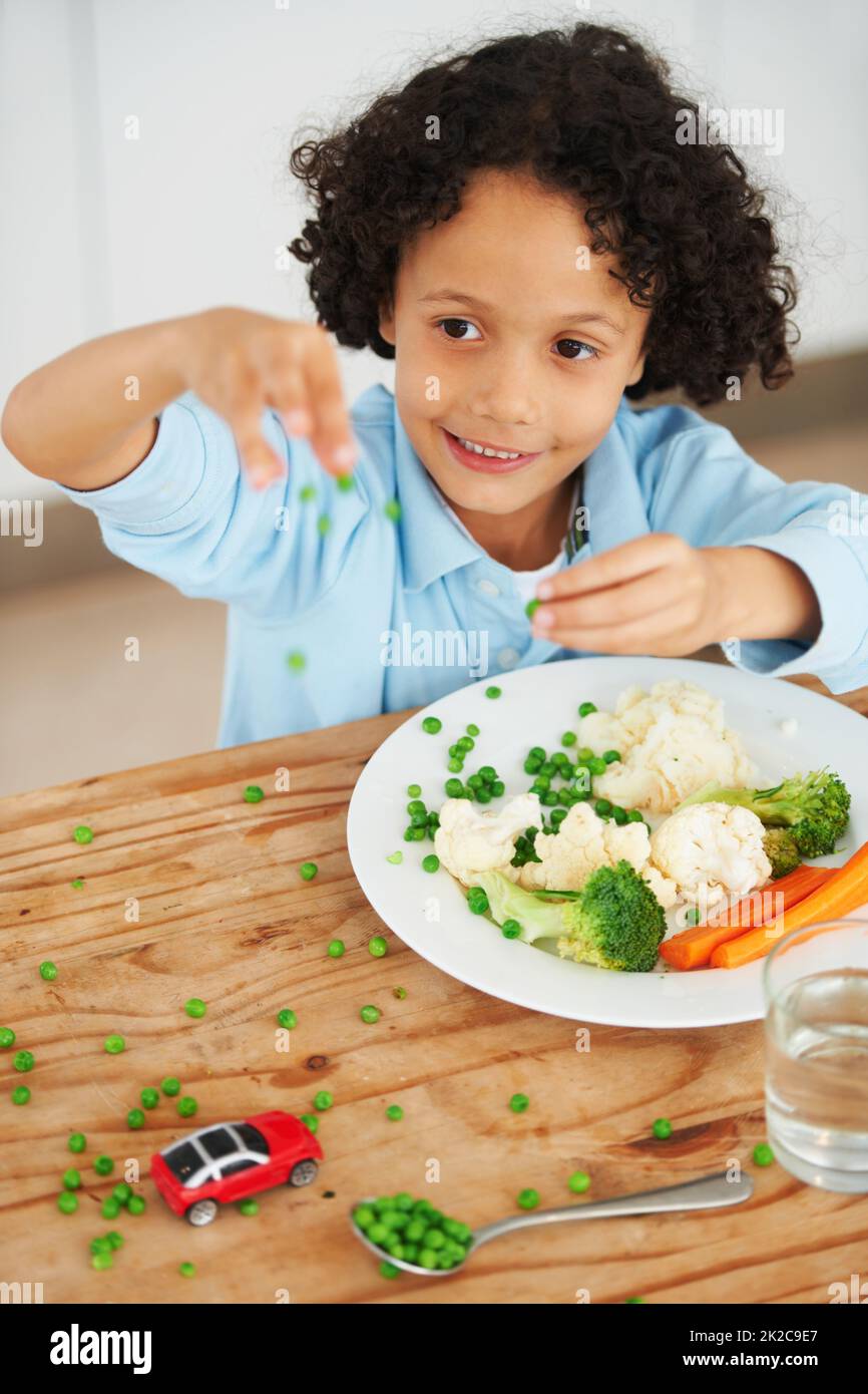 Spielen mit dem Essen. Ein süßer Junge warf Erbsen von seinem Teller über den Tisch. Stockfoto