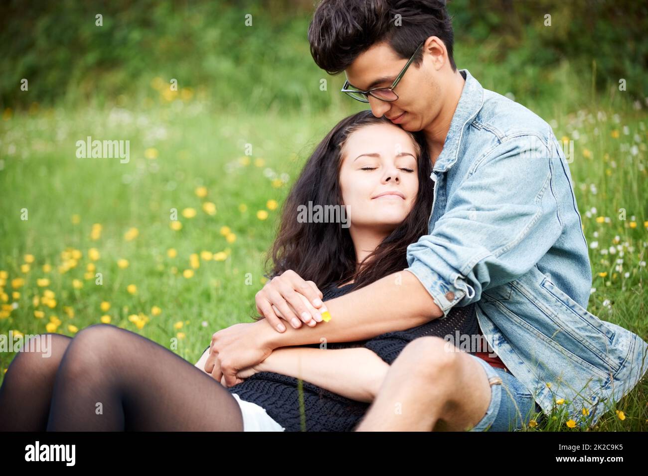 Eine süße Bindung teilen. Junges Paar, das liebevoll in einem Frühlingsfeld zusammensitzt. Stockfoto