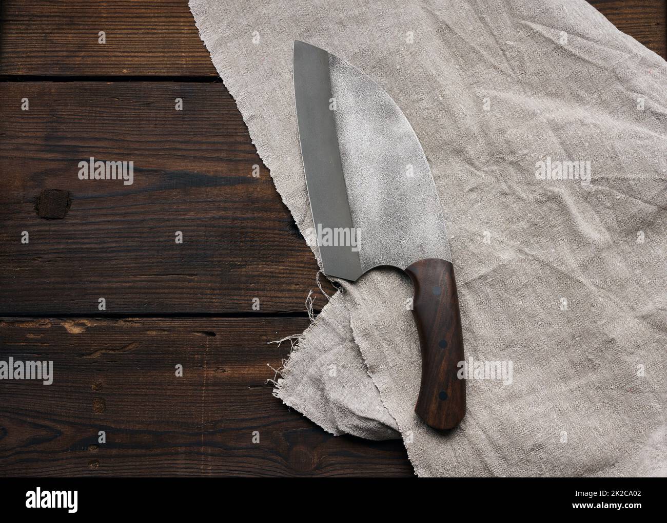 Scharfes Küchenmesser aus Metall in einem Holzgriff auf einem braunen Tisch aus Brettern Stockfoto