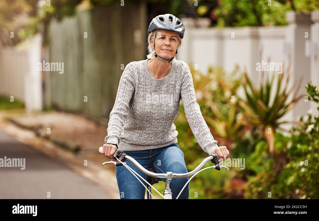 Nur eine sanfte Fahrt die Straße hinunter. Porträt einer fröhlichen älteren Frau, die draußen in einem Vorort alleine auf einem Fahrrad reitet. Stockfoto