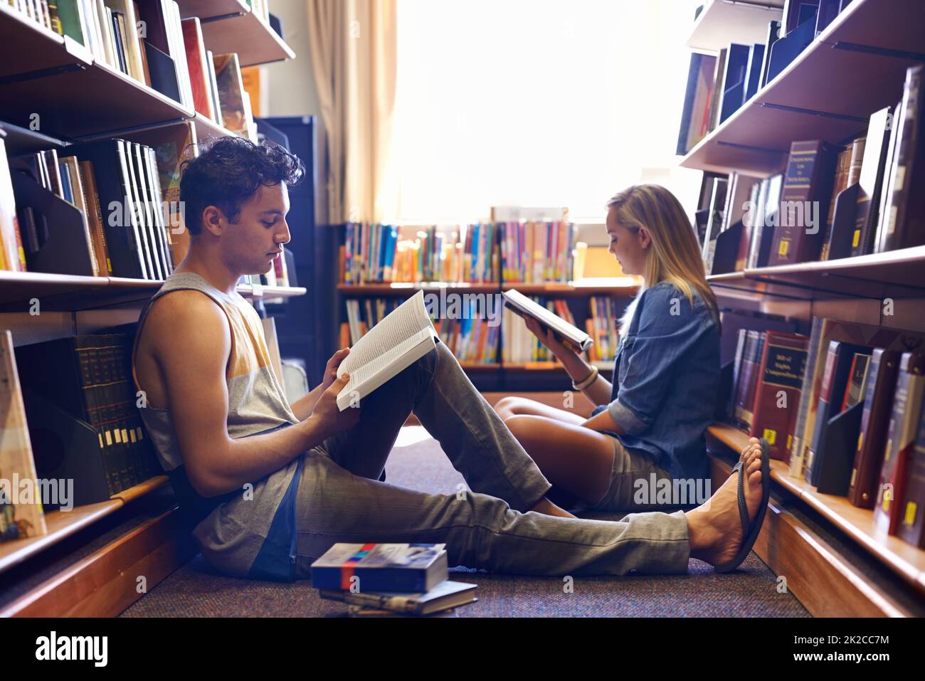 Gemeinsam studieren, aber getrennt. Zwei Studenten lesen in der Bibliothek separate Lehrbücher. Stockfoto