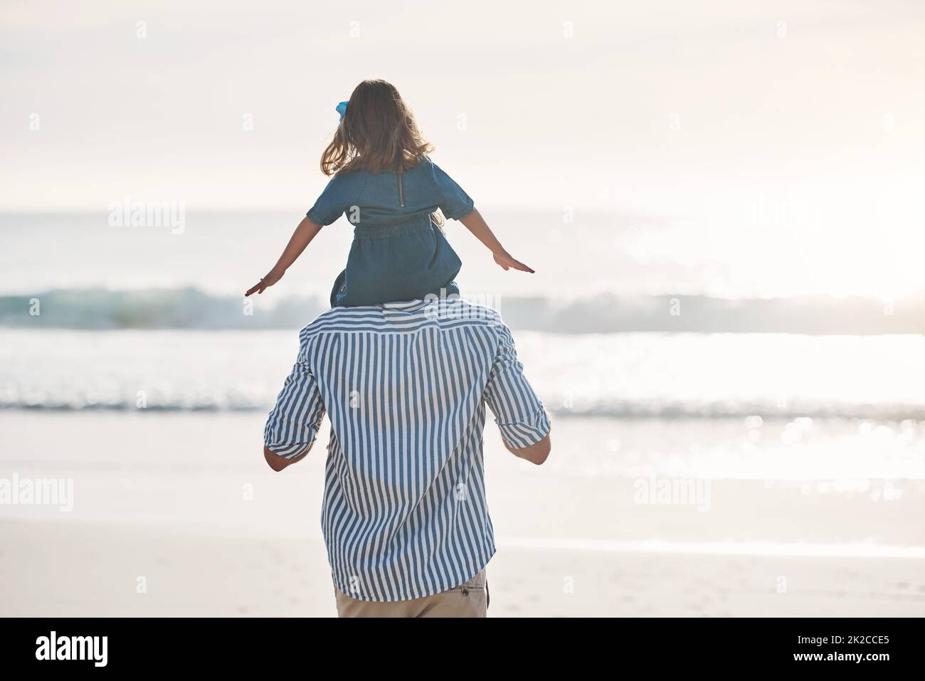 Daddys kleines Mädchen. Rückansicht eines unverkennbaren Vaters, der seine junge Tochter während eines schönen Tages am Strand auf den Schultern trägt. Stockfoto