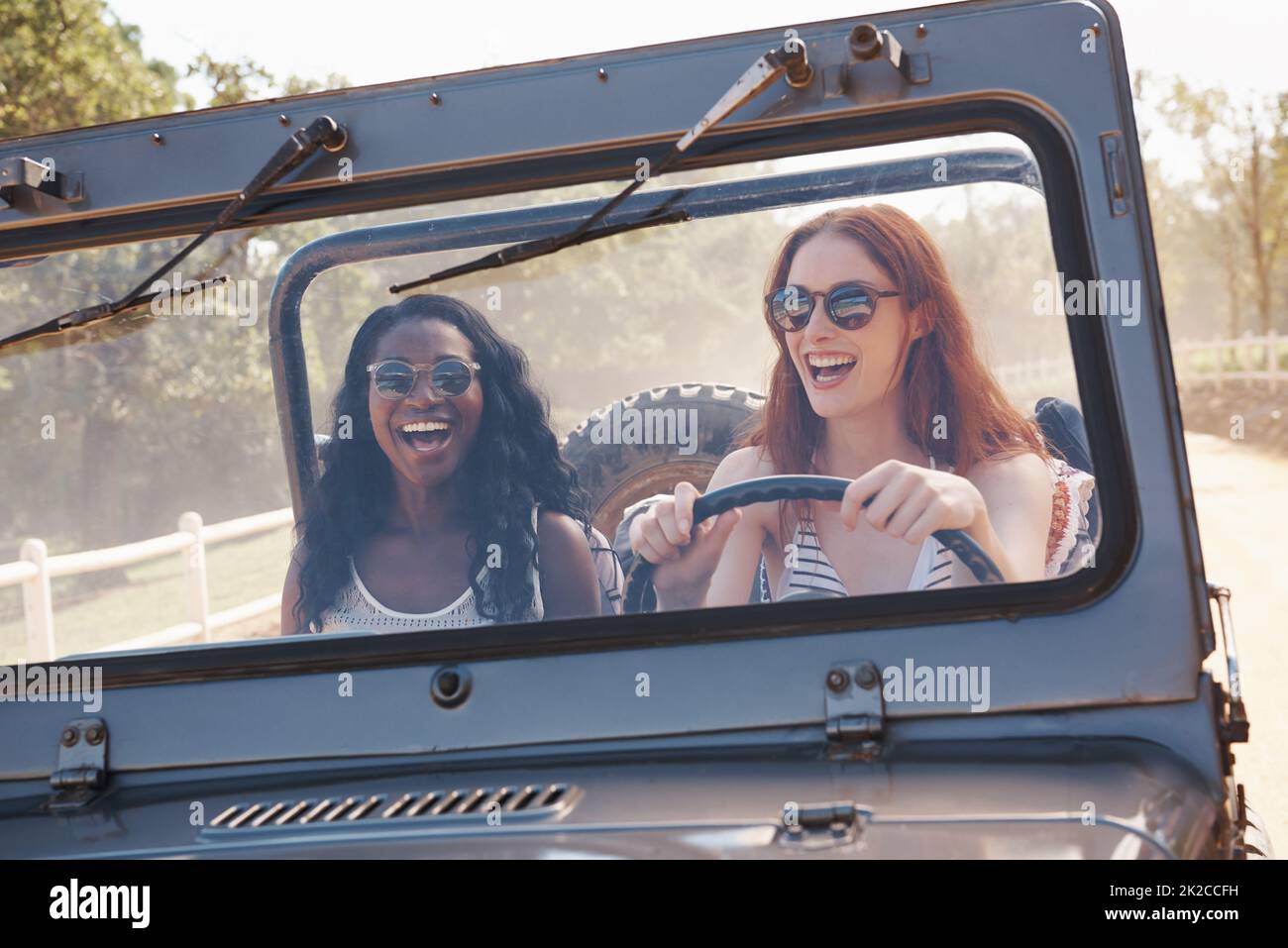 Spaß ist unser Treibstoff. Kurzer Schuss von zwei lachenden Frauen, die auf einer unbefestigten Straße fahren. Stockfoto