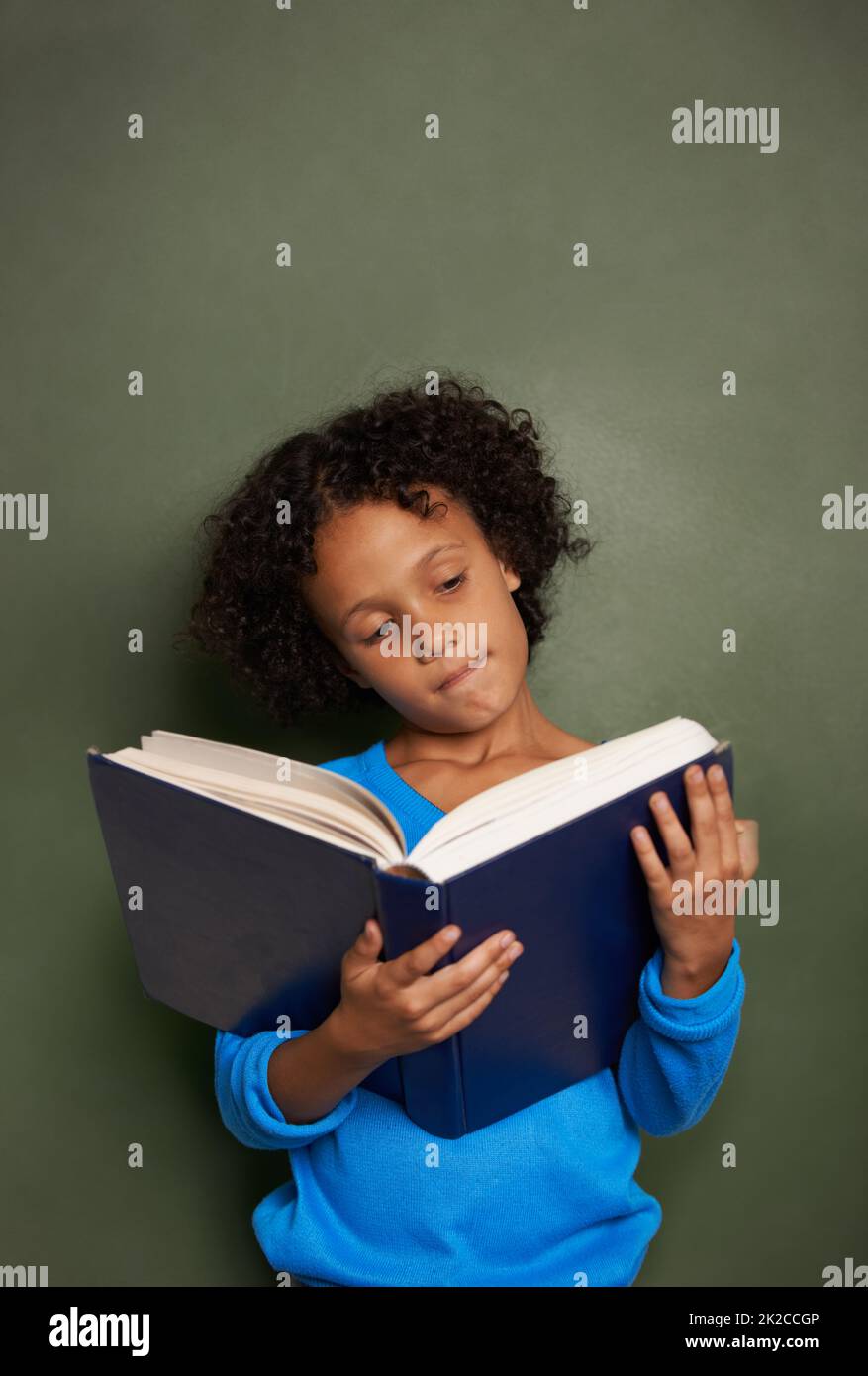 Es gibt keinen so treuen Freund wie ein Buch. Ein junger ethnischer Junge liest ein Buch, während er vor einer Tafel steht. Stockfoto