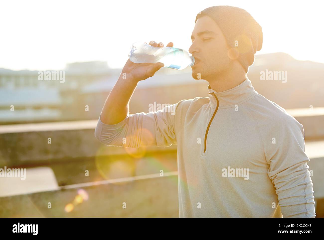 Schnell laufen, tief trinken. Aufnahme eines jungen Joggers, der während eines Laufs in der Stadt Wasser trinkt. Stockfoto