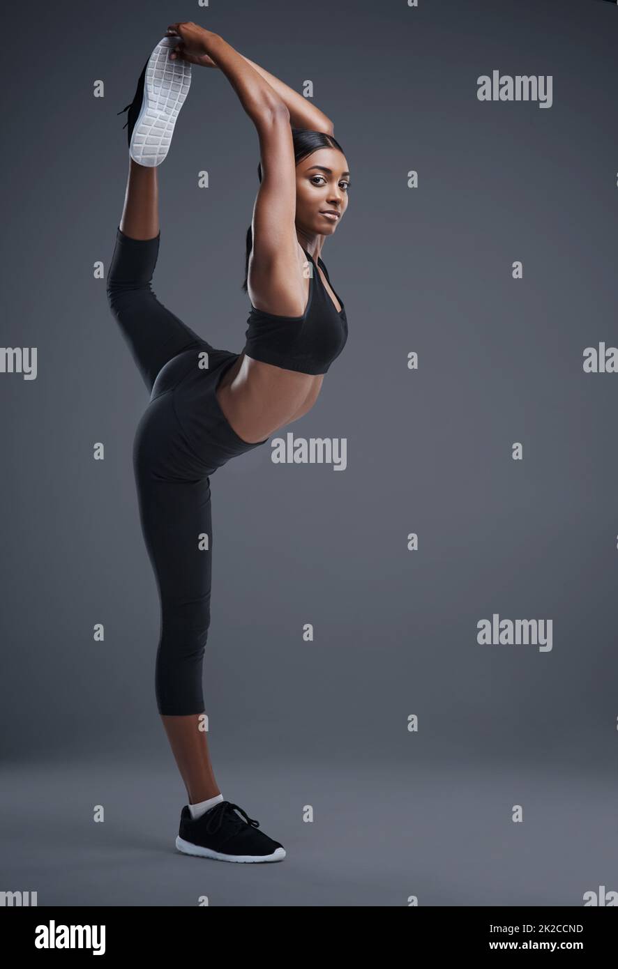 So wild wie sie flexibel ist. Studioportrait einer sportlichen jungen Frau, die ihren Körper vor einem grauen Hintergrund streckt. Stockfoto